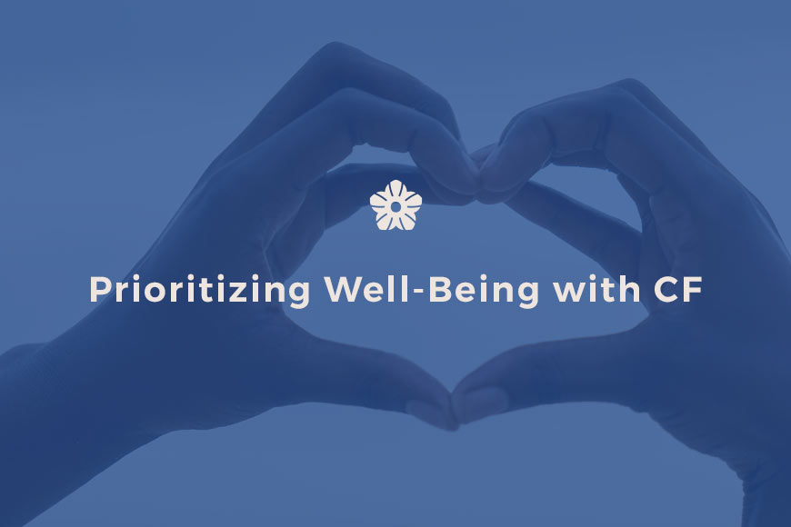 Photo of hands making a heart shape with blue overlay and off white sans-serif type with Filotimo flower above