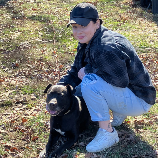HardshipSupport_MonicaBritt Woman kneeling with her dog in the grass.