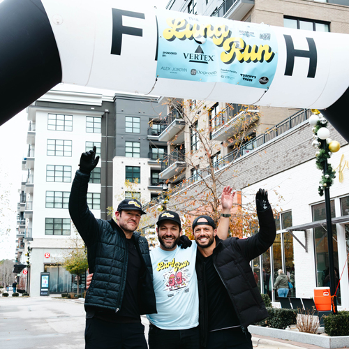 Three smiling men posing with their arms around each other beneath the finish line arch at the Lung Run charity event.